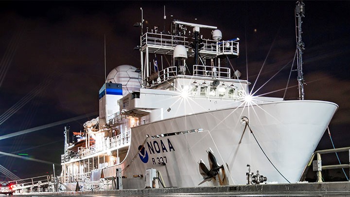 The NOAA ship Okeanos Explorer as seen from a dock, with the night sky in the background.