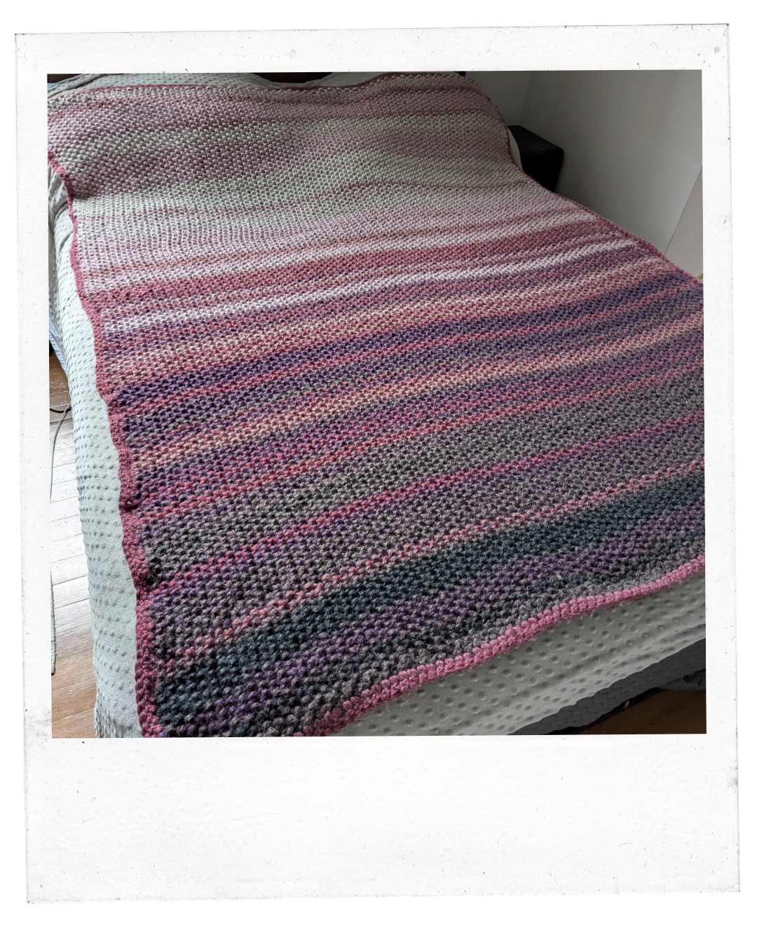 a large blanket covers a bad comprised of rows of shades of purples and grays