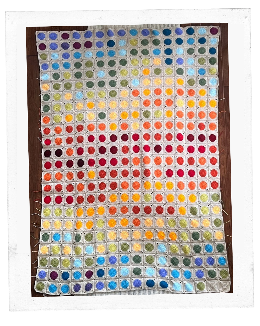 Blanket made up of rows of small circles of varying shades of blues, reds, yellows, and greens.