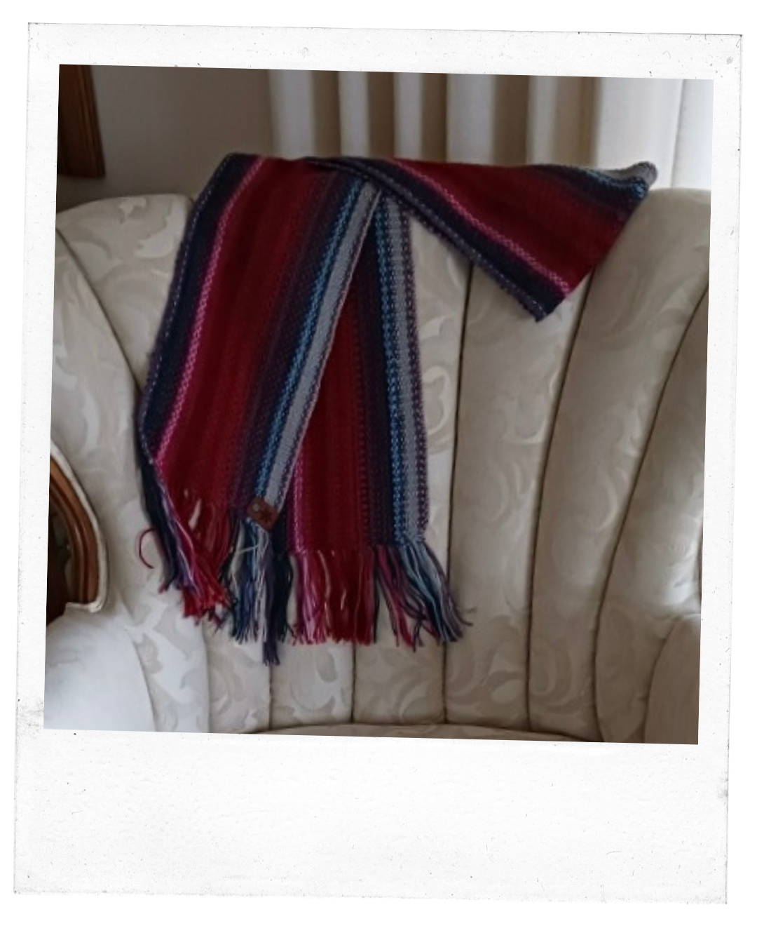 handcrafted scarf consisting of rows of varying shades of reds and blues lays across the back of a white chair