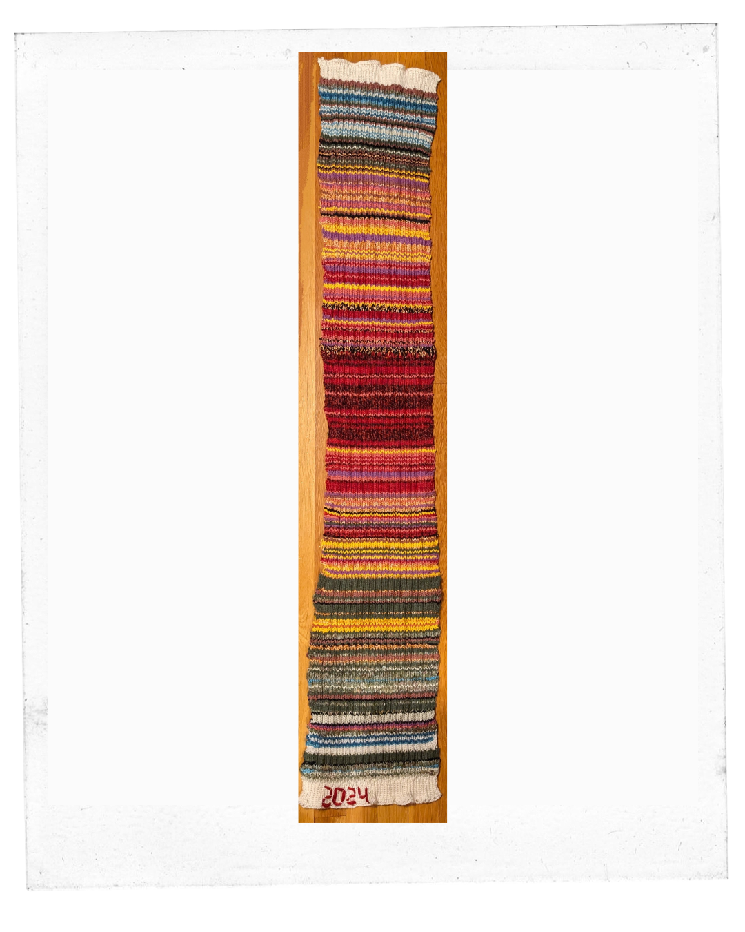 photo of temperature scarf consisting of lines of reds, yellows, browns, grays. 2024 stitched in the border. 