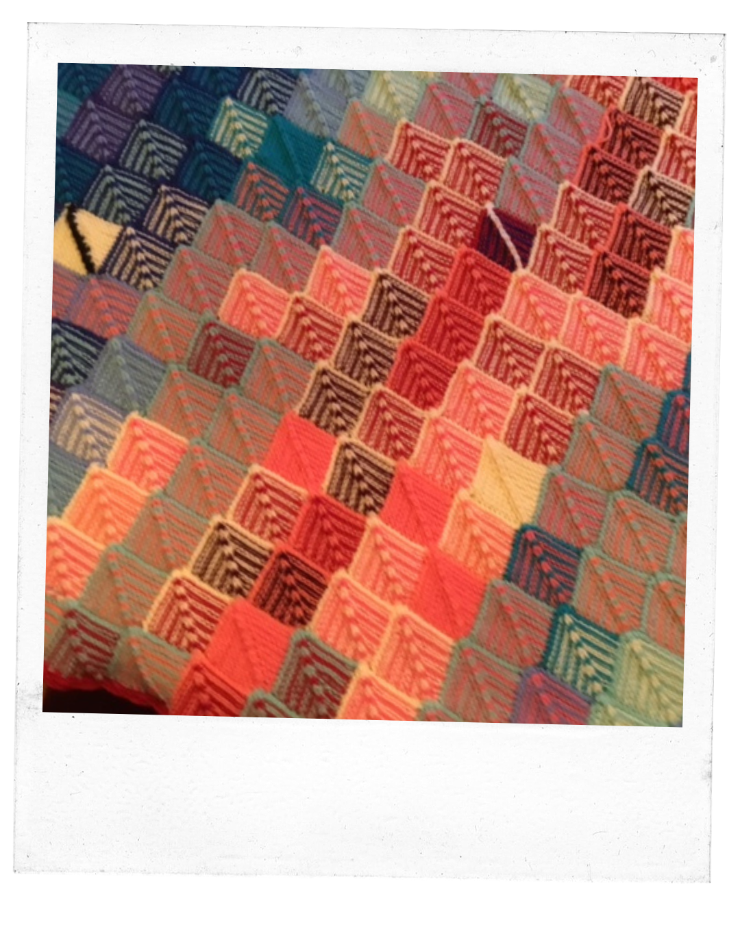 Close up of a blanket consisting of garter stitched mitered squares, sort of looks like scales made of lines of pinks, reds, and blues