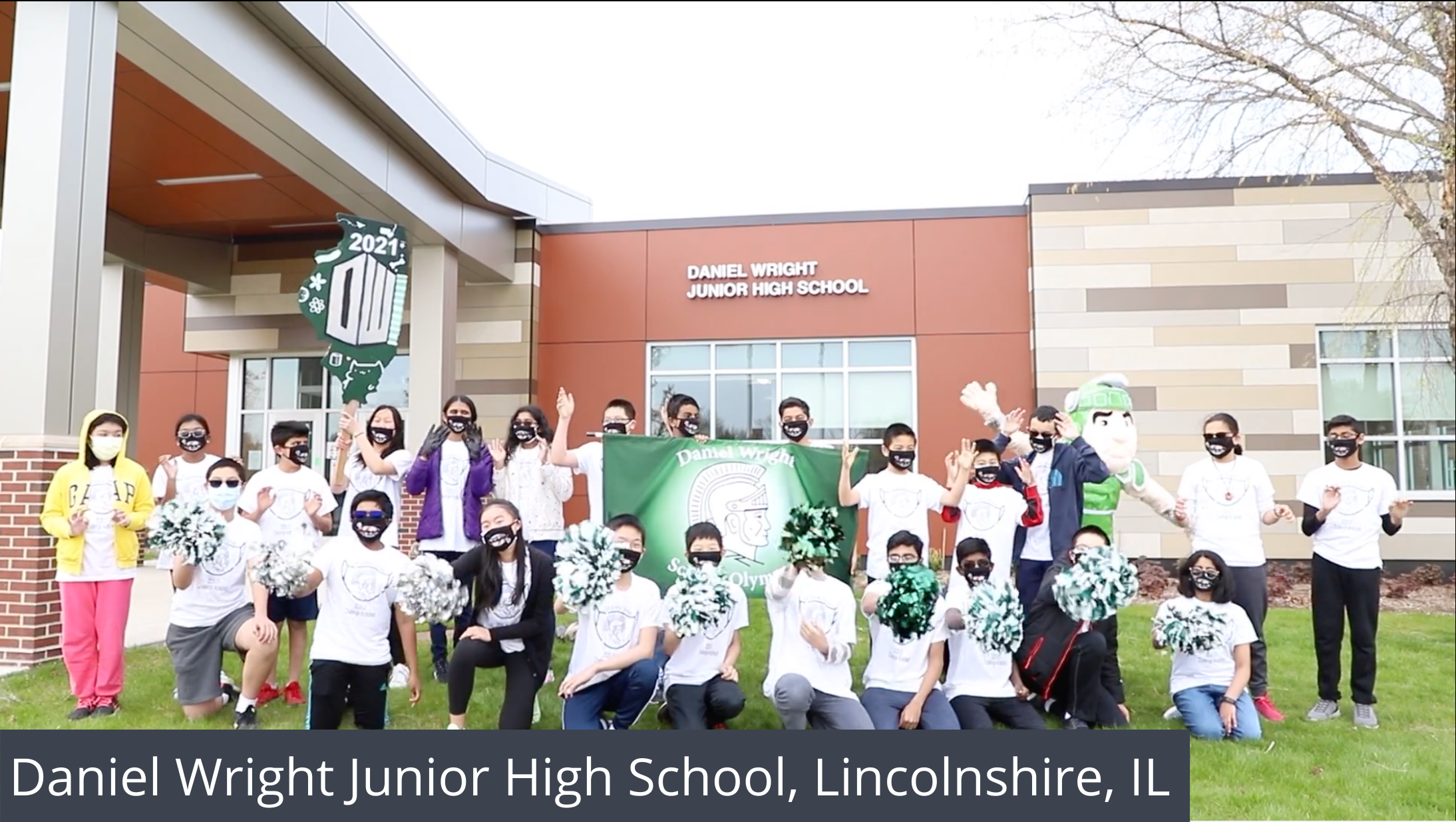 A group of students stand in front of their school with a banner and pom-poms.