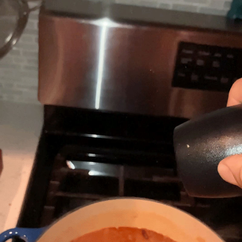 In slow motion, small flecks of pepper rise up into the air above a pot of simmering soup.