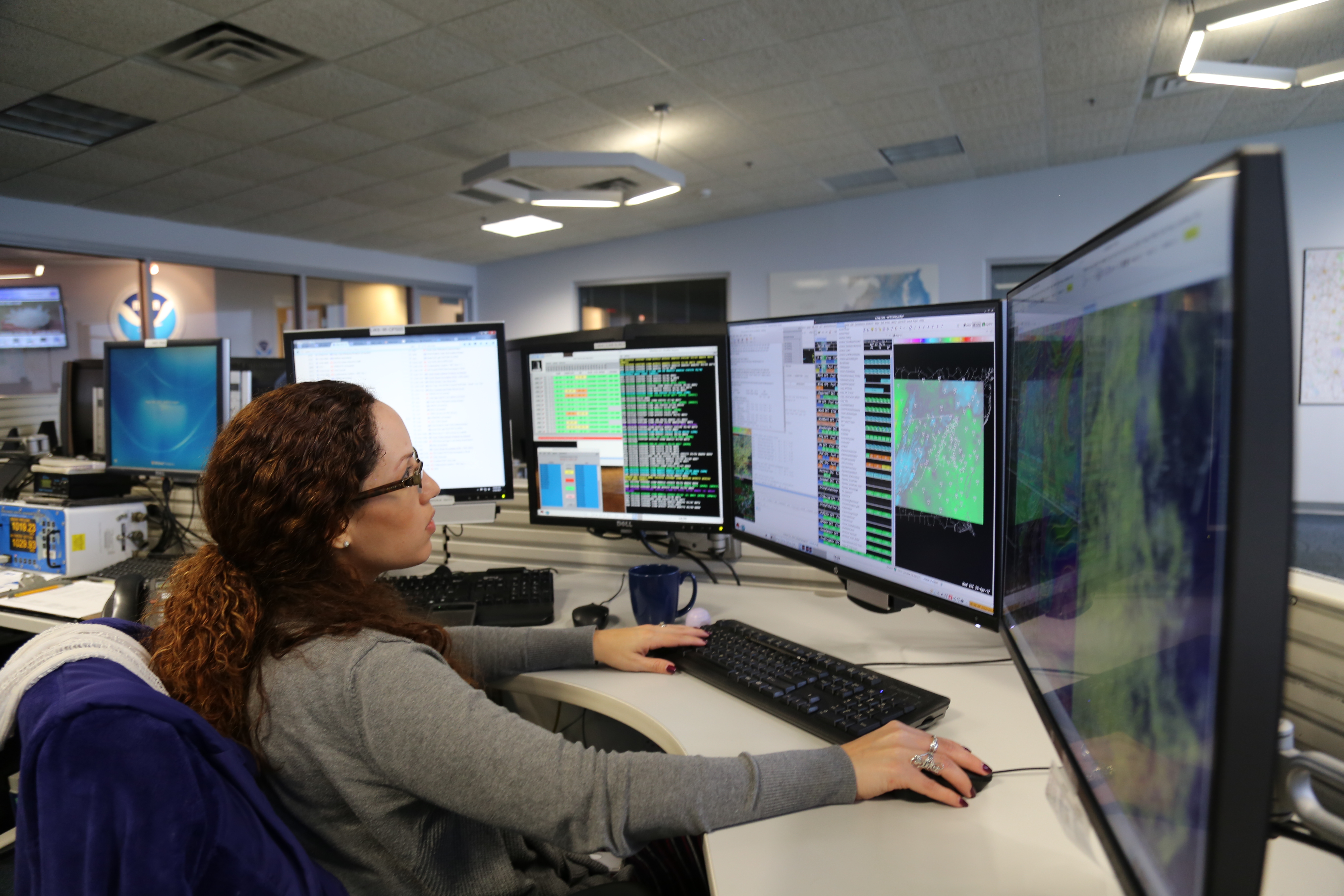 forecaster seated and working at a bank of four computer screens