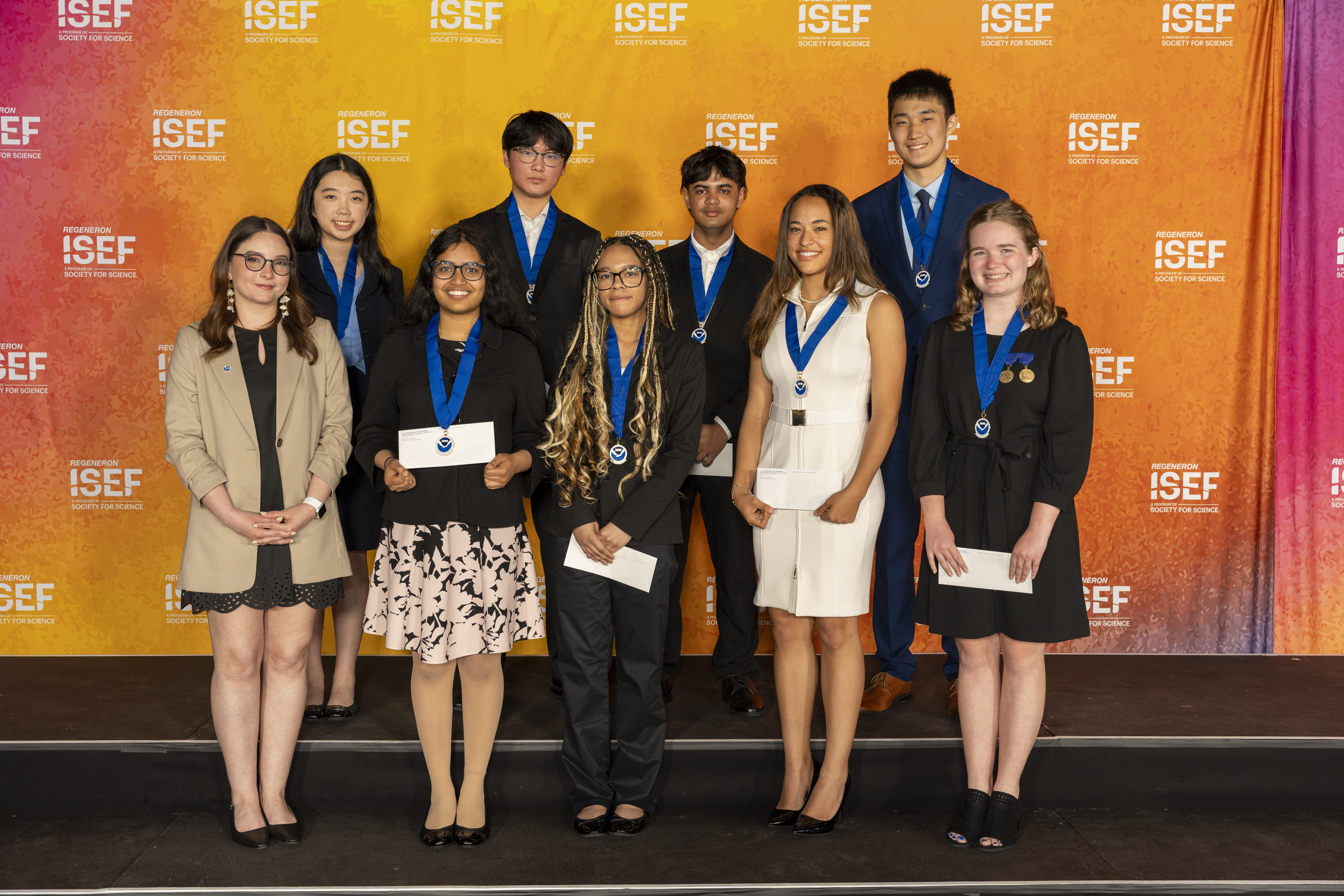A group of nine young adults pose for a group photo in front of a backdrop with the ISEF logo.