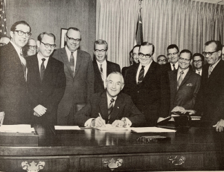 Secretary of Commerce Maurice H. Stans signs the department orders needed to put NOAA in operation on October 3, 1970. Dr. White is standing over Sec. Stans’ left shoulder.