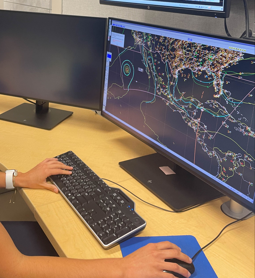 Delián looks at a large computer monitor, which displays hundreds of data points overlaid on simple outline of the southern United States, Caribbean, and Central America.