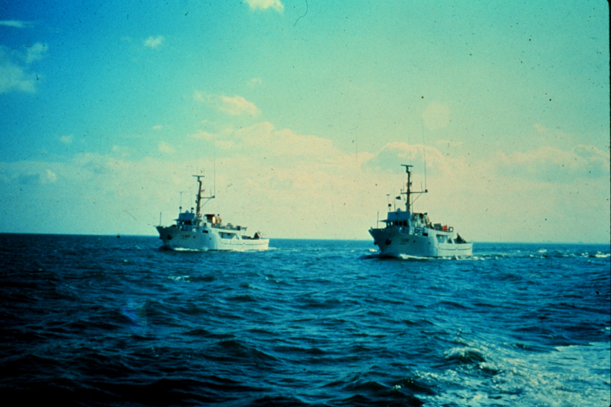 NOAA Survey Ships Rude & Heck next to each other in the ocean with nothing but sky behind them.