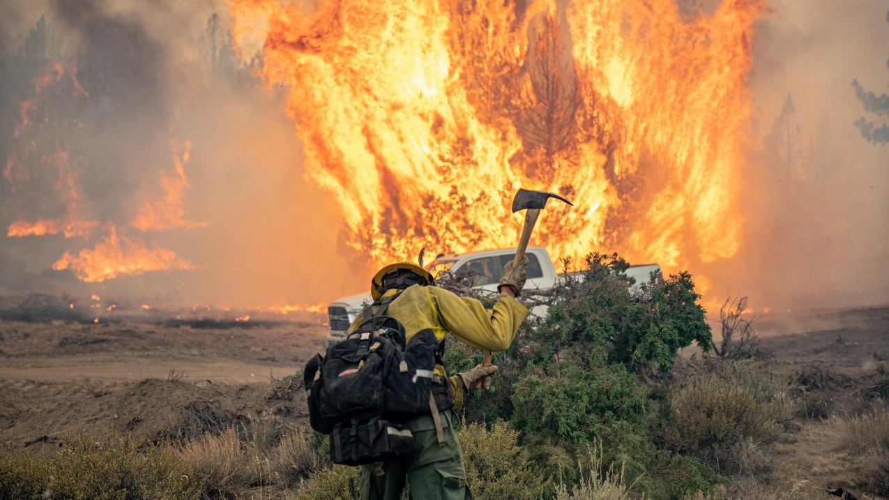 Firefighter with axe with blazing fire in the background.