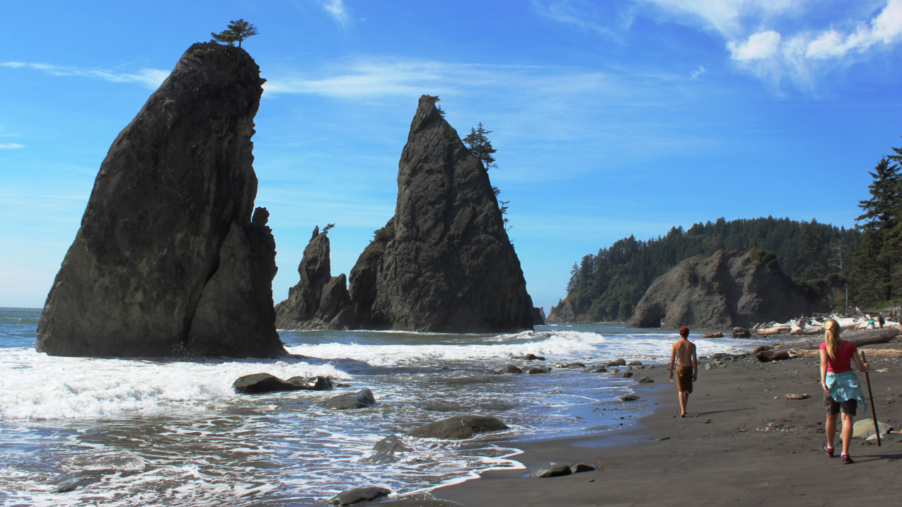 People walking on a beach with rocks coming out of the water.
