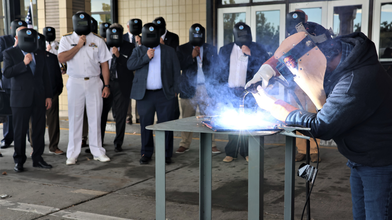 Photo of welder from Thoma-Sea Marine Constructors, LLC, welds the initials of Discoverer's sponsor, Second Gentleman Douglas C. Emhoff, onto a steel plate that will be incorporated into the ship in keeping with maritime tradition.