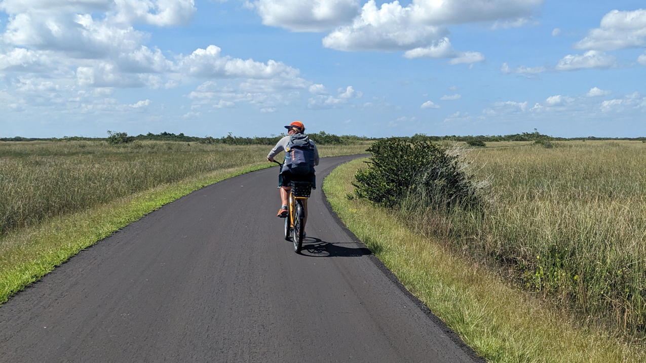 Ellie bikes on a flat blacktop pathway and looks at the distance to her side.