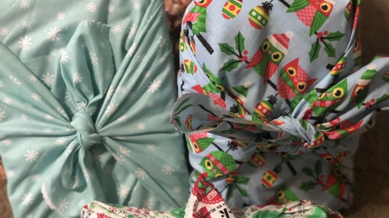 Four holiday gifts are neatly assorted on the ground, wrapped in holiday patterned cloth instead of wrapping paper.