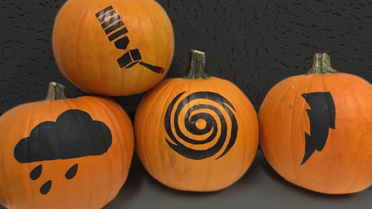 Four pumpkins with black icons painted on featuring a raincloud, a GOES-R satellite, a hurricane, and lightning.
