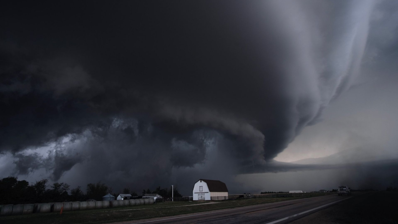The dark cloud of a supercell thunderstorm stretches across thee sky over a barn in Kansas.