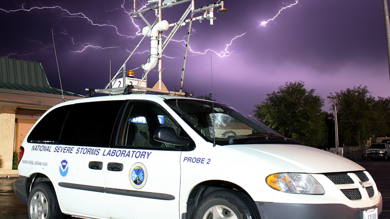 A National Severe Storms Laboratory observing vehicle takes measurements as lightning strikes in the background. Credit: NSSL.