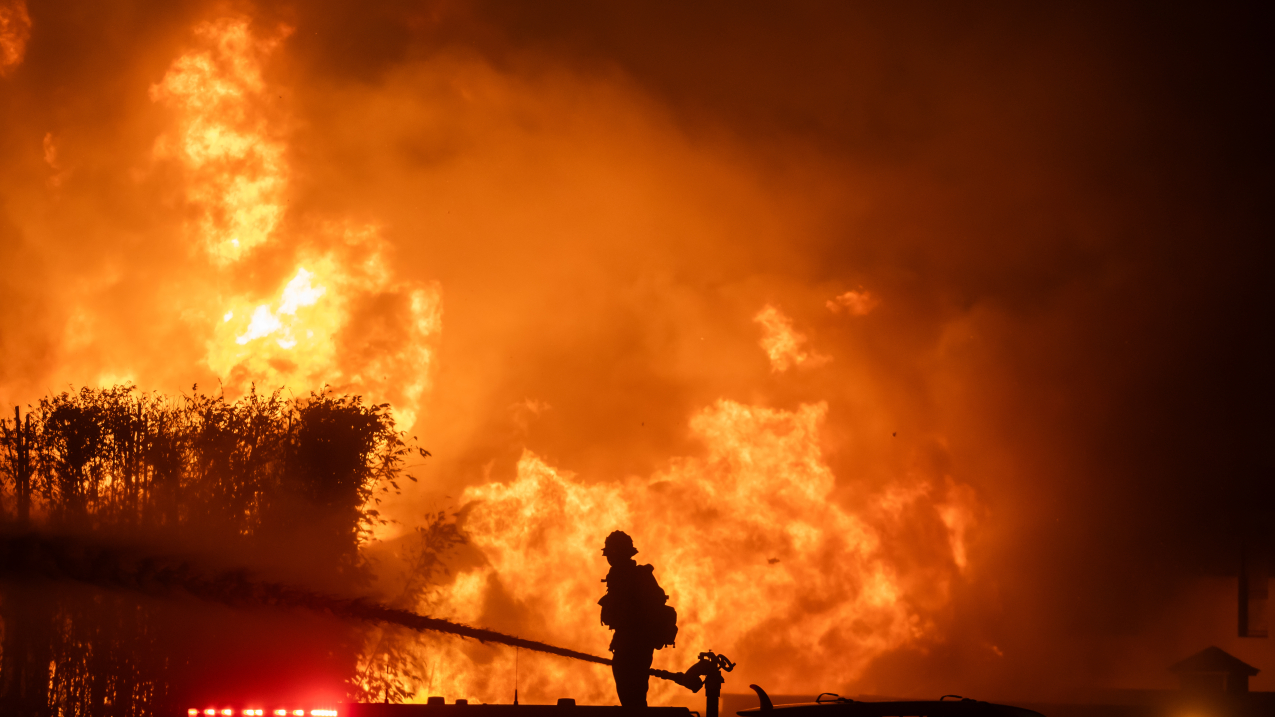 January 8, 2025: A firefighter stands on top of a fire truck to battle the Palisades Fire while it burns homes on the Pacific Coast Highway in Los Angeles, California. Dry conditions and near-hurricane-force Santa Ana winds contributed to the rapid spread of wildfires in the area.