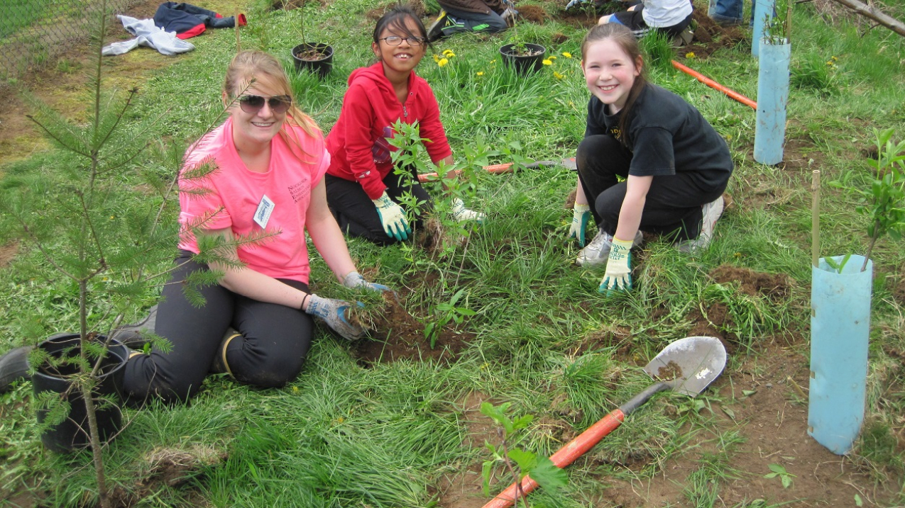 2 students planting trees with an adult during a restoration field trip