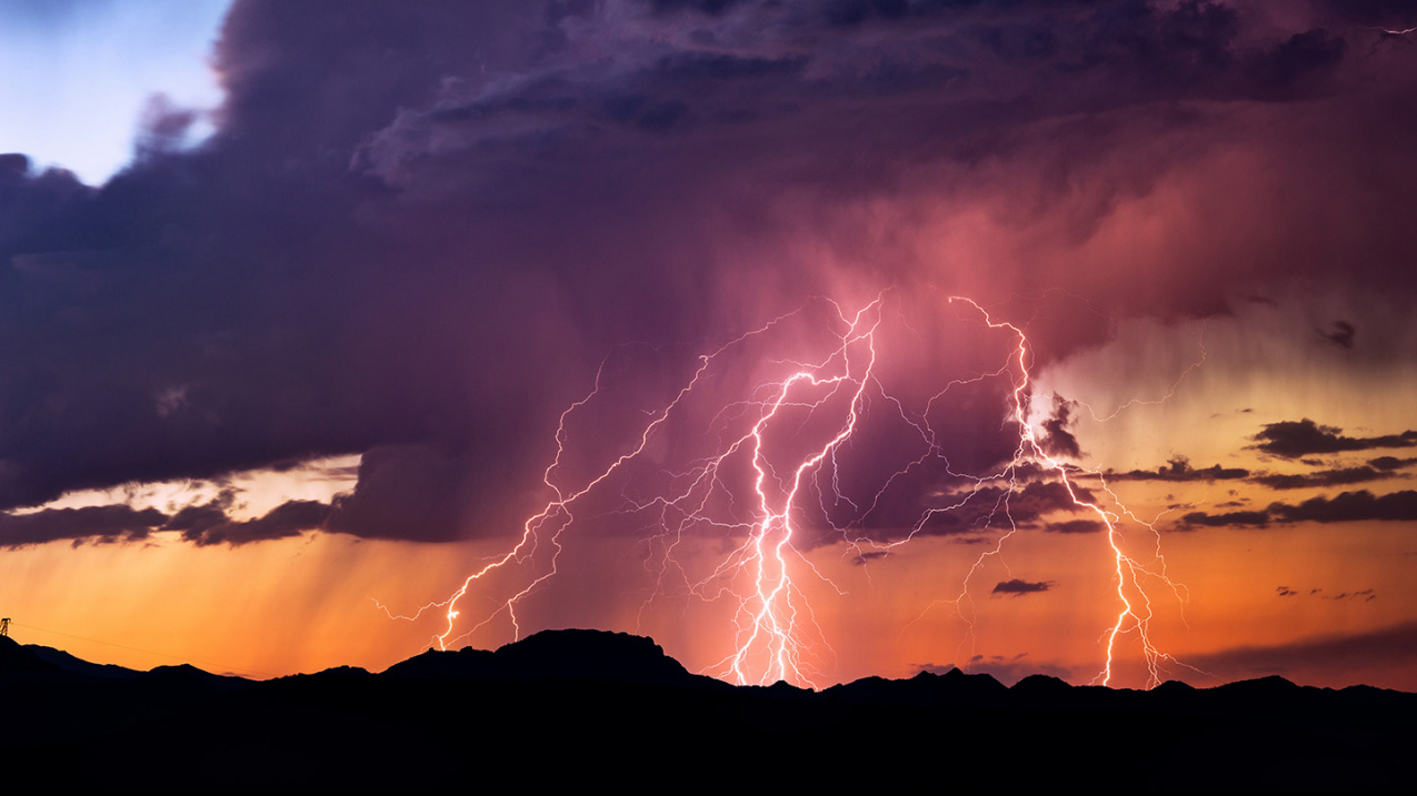 Powerful lightning bolts strike from a sunset thunderstorm in the Arizona desert.