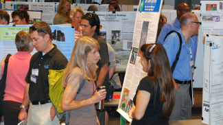 People talk with each other and look at posters in a busy poster hall.