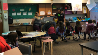 A group of students in a classroom watch as two instructors point to an aquarium tank. The phrase “You Matter” is written in large letters on the classroom wall. 