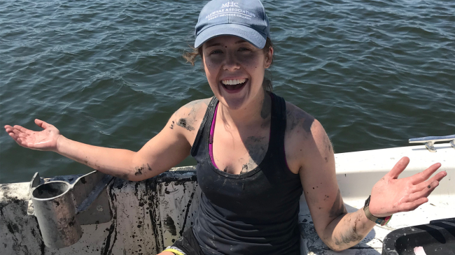 Person sits covered in mud with water in the background