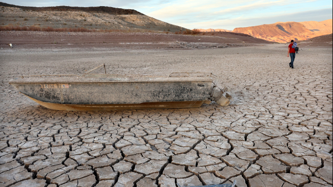 A person walks past a formerly sunken boat resting on a now-dry section of lakebed at Lake Mead on May 10, 2022.