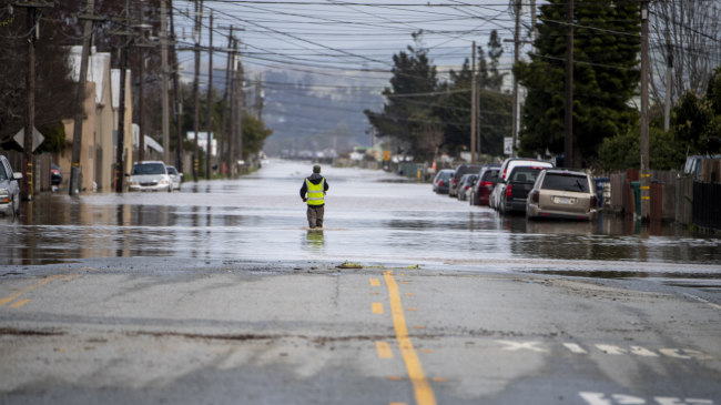 Photo of a man walks through floodwaters downstream from a levee break along the Pajaro River in Monterey County, California. Heavy rain from an atmospheric river caused the levee to fail. March 12, 2023. Credit: California Department of Water Resources.