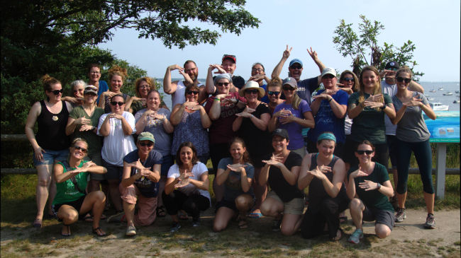 A group of people stands together looking at the camera with their hands in different signs.