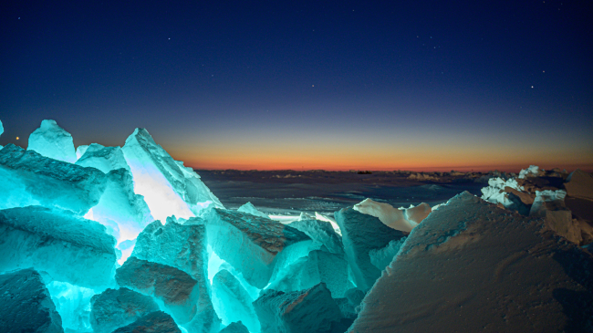 In the early morning hours, sunlight returns to the Arctic in spring, illuminating sea ice in a blue glow, after months of winter darkness. 