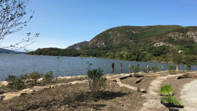 A gravel path winds through dirt by a river under a blue sky.