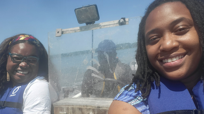 A woman and a girl wearing blue life vests on a boat in a river.