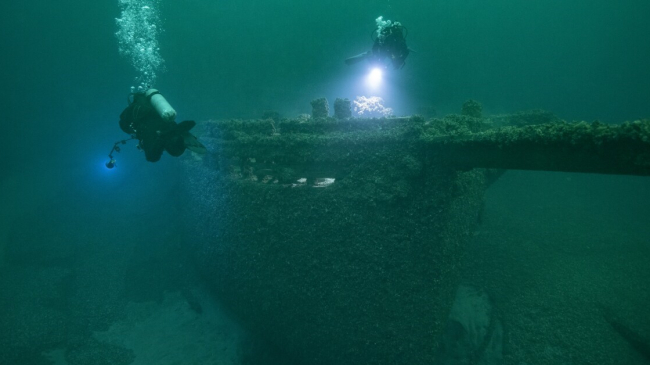 Photo showing divers exploring the wreck of schooner St. Peter, which lies in 117 feet of water in Lake Ontario National Marine Sanctuary. St. Peter was loaded with coal when it sank in a storm near Pultneyville in Wayne County, New York, in October 1898.
