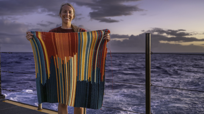NOAA Ocean Exploration Internship Program Coordinator Jesse Gwinn on the fantail of NOAA Ship Okeanos Explorer with her in-progress bathymetry blanket, which illustrates ocean depth data collected during the Beyond the Blue: Johnston Atoll Mapping 2 expedition.