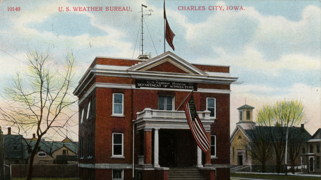 Postcard of the U.S. Weather Bureau Building at Charles City, Iowa. c. 1900. Note the Weather Forecast Flag system flags flown on the flag pole mounted on the roof. They appear to be the blue flag with a black pennant above, indicating a forecast of higher temperatures and rain.
