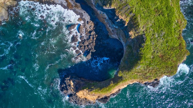 Aerial view of a grass covered cliff that wraps around a rocky beach
