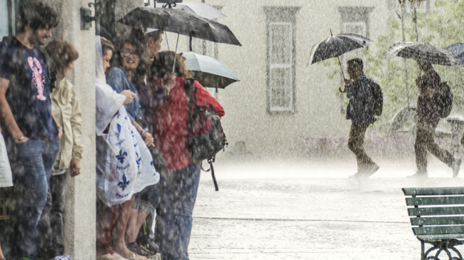 Stock photo of people on the street in Quebec, Canada, taking shelter from a heavy rainstorm, while three people in the background brave the elements with umbrellas.