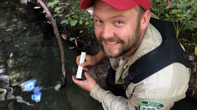 A NOAA Veterans Corps member working outside in a body of water. He is looking directly at the camera and posing for the photo.