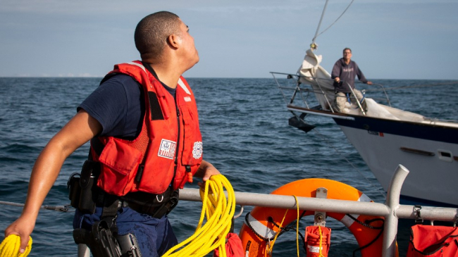 Petty Officer 3rd Class Wayne Ballard, a U.S. Coast Guardsman, throws a rope across to stranded sailor during a rescue in the Gulf of Mexico, Dec. 19, 2019. This rescue was one of more than 400 that were assisted by NOAA satellites.