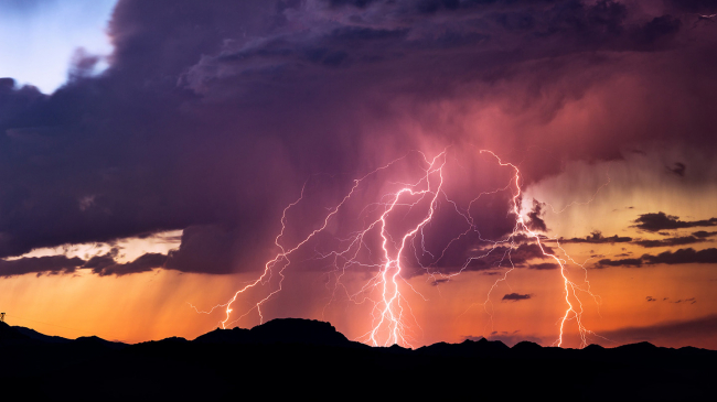 Powerful lightning bolts strike from a sunset thunderstorm in the Arizona desert.