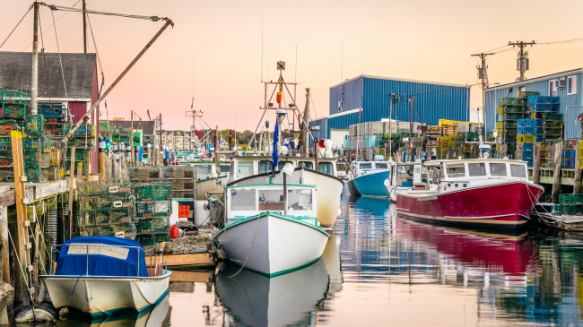 Harbour with colourful fishing boats at sunset. Lots of lobster traps are piled on the wooden piers. Great reflection in the calm water. Portland, Maine.