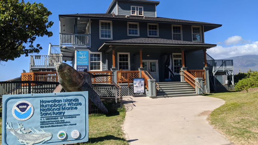 Hawaiian Islands Humpback Whale National Marine Sanctuary Visitor Center building in background with humpback whale sculpture and site placard in the foreground.
