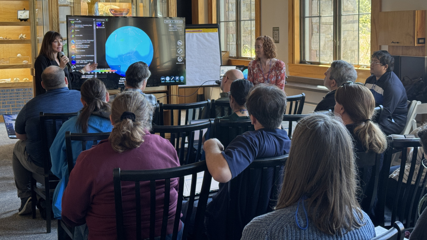 A presenter shows examples of datasets on SOS Explorer software on a large LCD display to a group of sitting participants at a workshop.