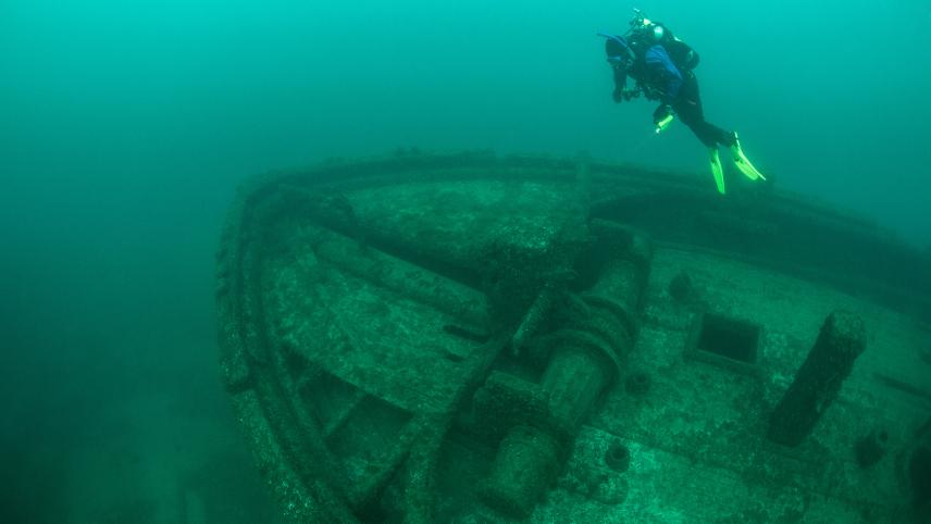 A diver observes a shipwreck at the bottom of a lake. 