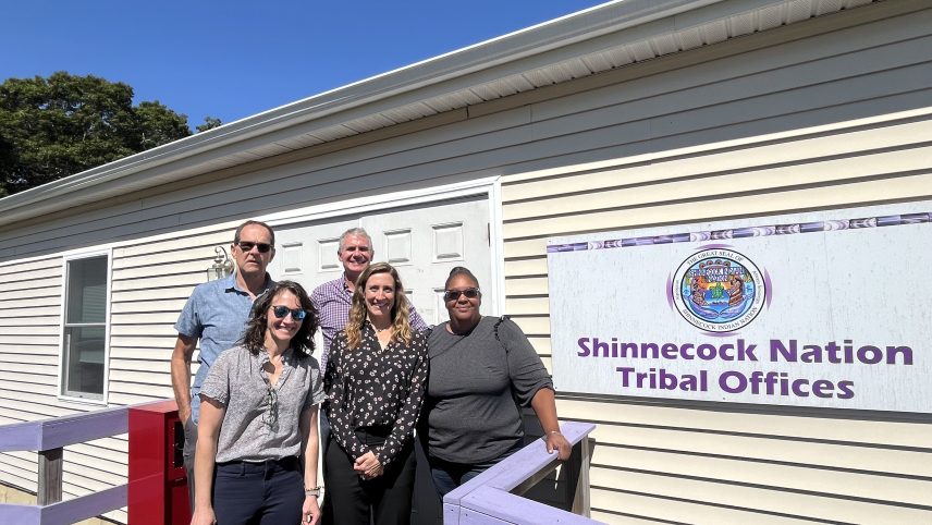 a group of people standing by a building with a sign reading “Shinnecock Nation Tribal Offices”