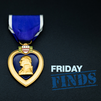 A Purple Heart medal lies on a black background. The medal features George Washington's head and Washington, DC's coat of arms and hangs from a purple ribbon with white borders.
