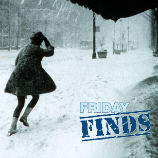 Black and white photo of a woman in a miniskirt and winter coat walking through the snow and holding her hat on her head.