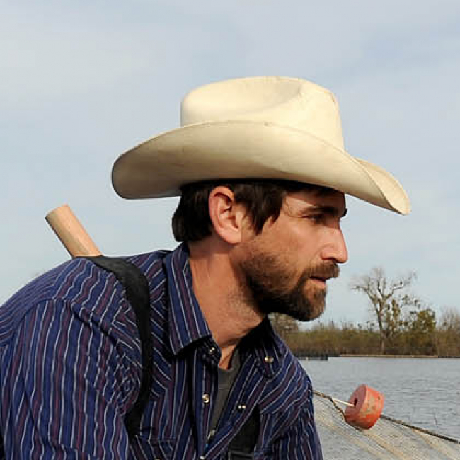 Jacob is wearing waders and pulling a seining net through shallow water.