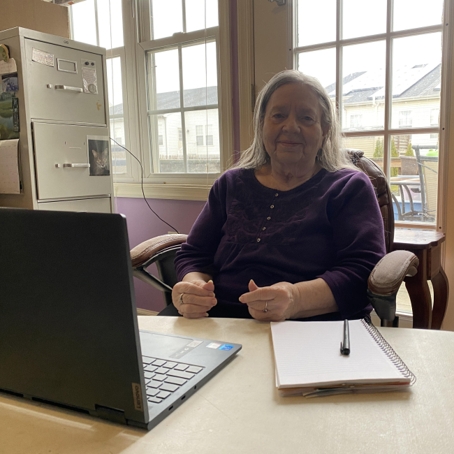 Maralyn Vorhauer sits in her home office with a laptop, notebook and pen in front of her.